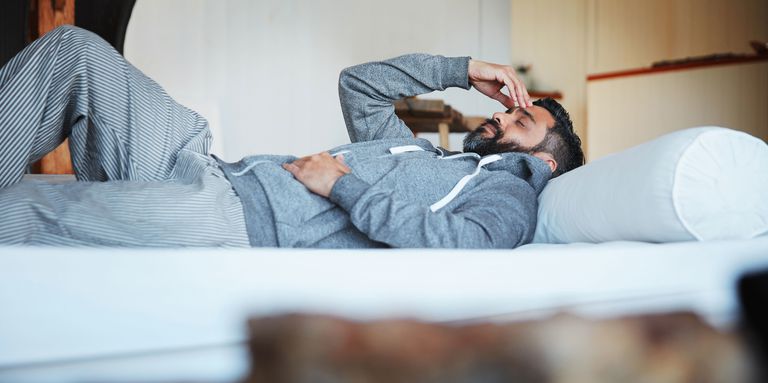 man struggling with sleep depravation laying on his back on the bed with his hands over his eyes
