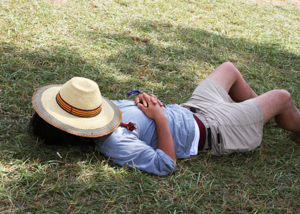 man taking a nap on the grass with hat on 