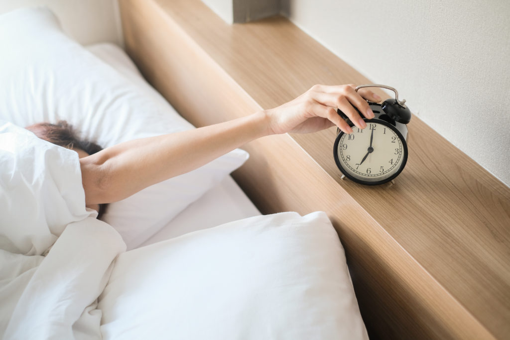 Person snoozing alarm clock in the morning